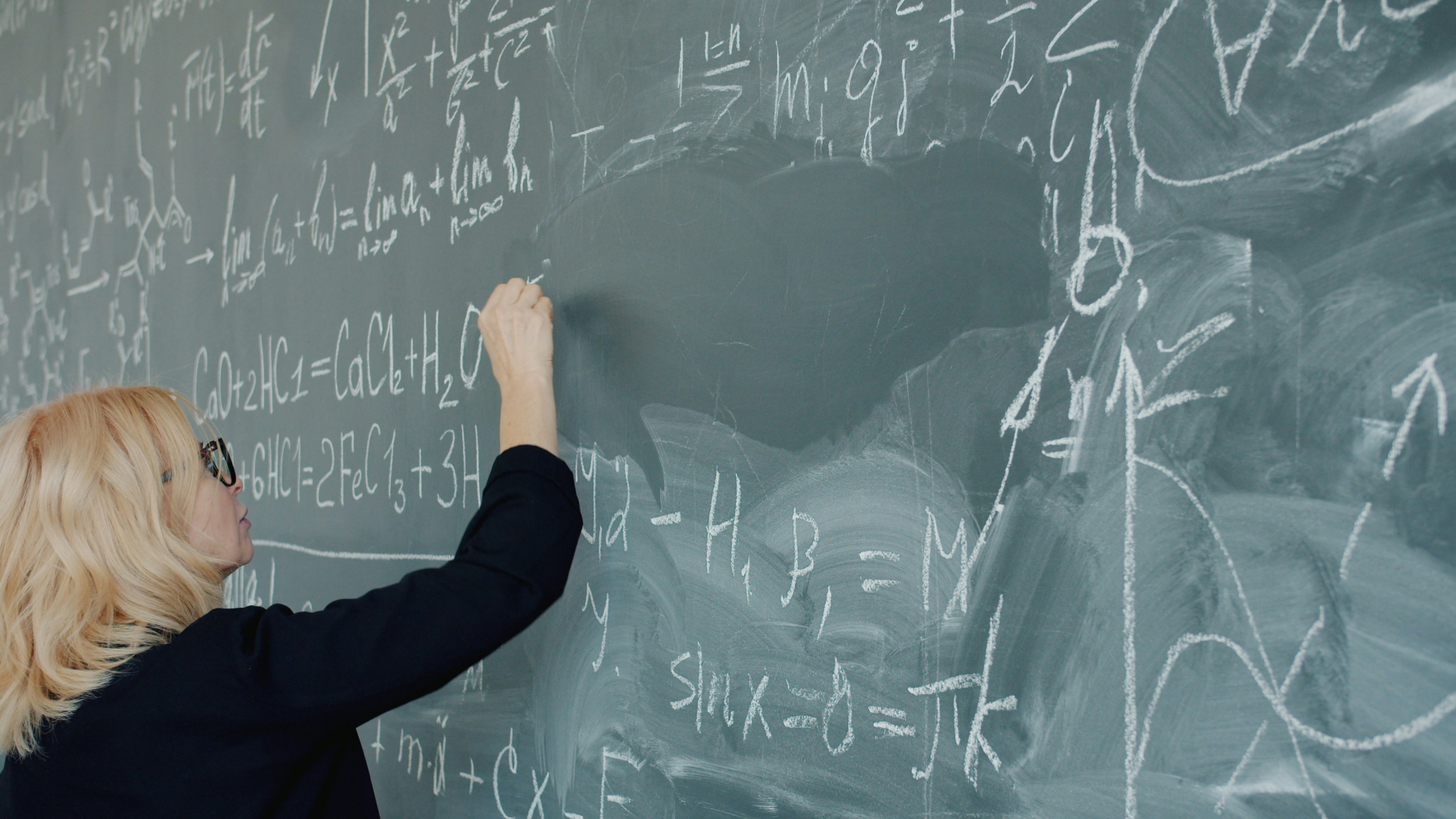 female chemistry teacher serious woman writing formulas on chalkboard teaching class. Modern education, smart people and lifestyle concept.